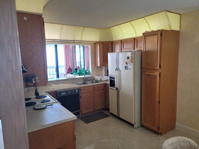 kitchen with black dishwasher, brown cabinetry, white fridge with ice dispenser, and a sink