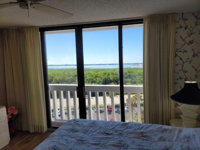 bedroom with multiple windows, a water view, a textured ceiling, and wood finished floors