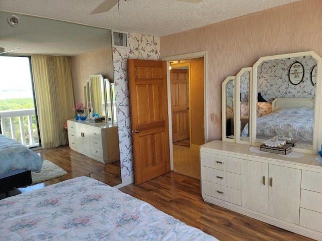 bedroom with visible vents, a textured ceiling, wallpapered walls, and dark wood-style flooring