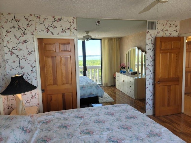 bedroom with access to exterior, visible vents, wallpapered walls, wood finished floors, and a textured ceiling