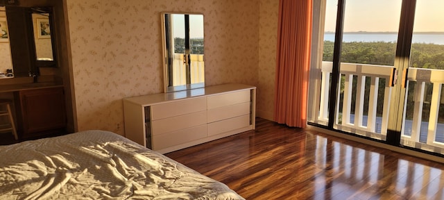 bedroom featuring multiple windows, wallpapered walls, a water view, and dark wood-style flooring