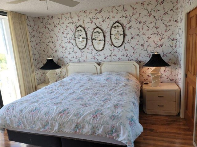 bedroom with multiple windows, a textured ceiling, wallpapered walls, and wood finished floors