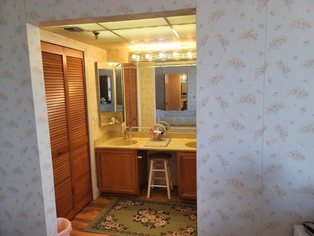 bathroom featuring wallpapered walls, double vanity, wood finished floors, a closet, and a sink