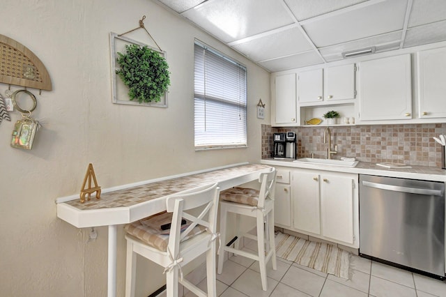 kitchen with a drop ceiling, backsplash, sink, stainless steel dishwasher, and white cabinetry