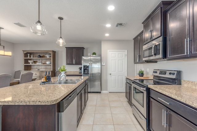 kitchen with appliances with stainless steel finishes, sink, decorative light fixtures, an island with sink, and light tile patterned flooring