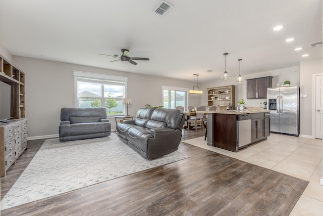 living room with built in shelves, light hardwood / wood-style flooring, and ceiling fan