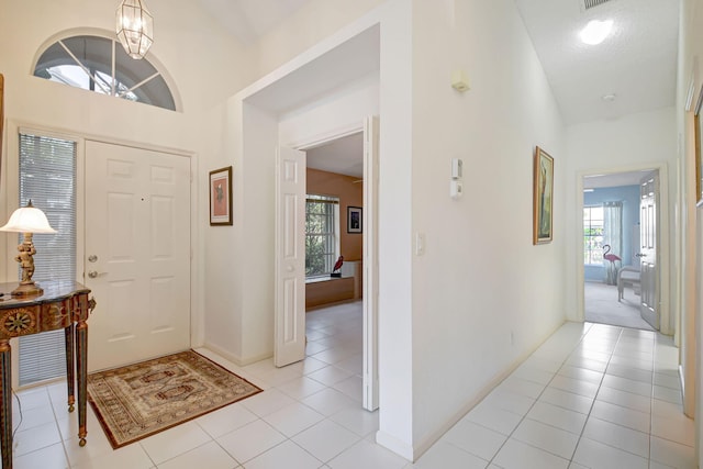 foyer with light tile patterned floors, an inviting chandelier, high vaulted ceiling, and plenty of natural light