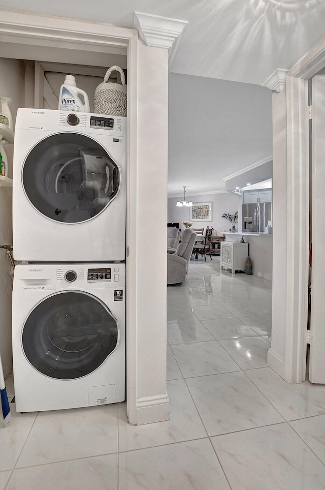 clothes washing area with crown molding, stacked washing maching and dryer, and an inviting chandelier