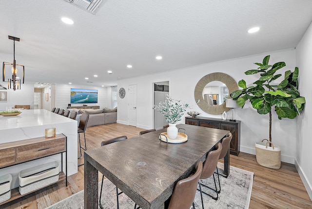 dining space with light hardwood / wood-style floors, a textured ceiling, and an inviting chandelier