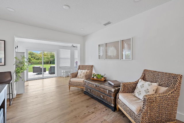 living area featuring ceiling fan, light hardwood / wood-style floors, and a textured ceiling