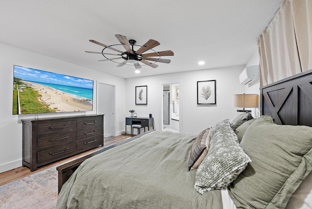 bedroom featuring a wall mounted air conditioner, light wood-type flooring, ceiling fan, and connected bathroom