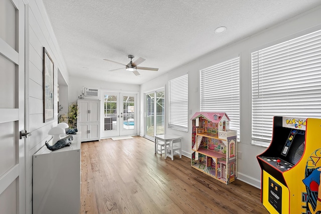 recreation room with ceiling fan, french doors, an AC wall unit, wood-type flooring, and a textured ceiling