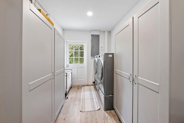 clothes washing area with cabinets, electric panel, a textured ceiling, separate washer and dryer, and light hardwood / wood-style floors