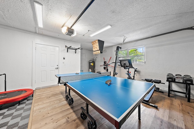 recreation room with electric water heater, wood-type flooring, and a textured ceiling