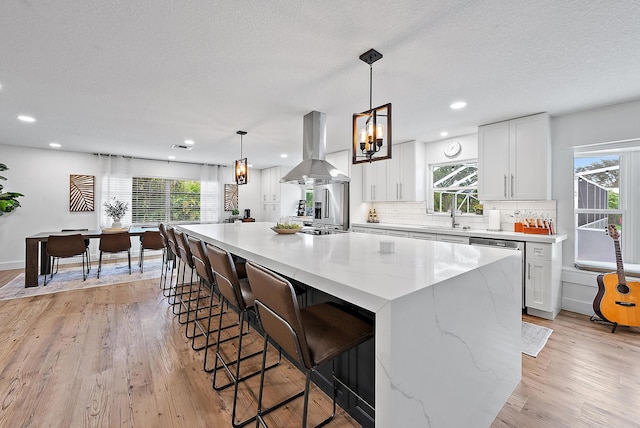 kitchen with white cabinets, a spacious island, light wood-type flooring, range hood, and plenty of natural light