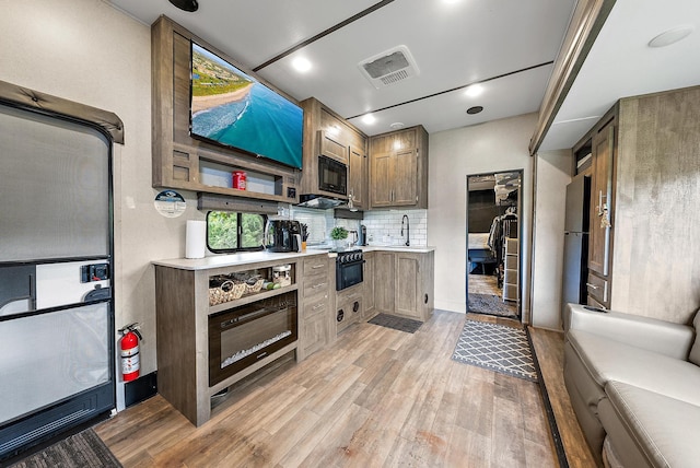 kitchen with black appliances, light hardwood / wood-style floors, sink, and backsplash