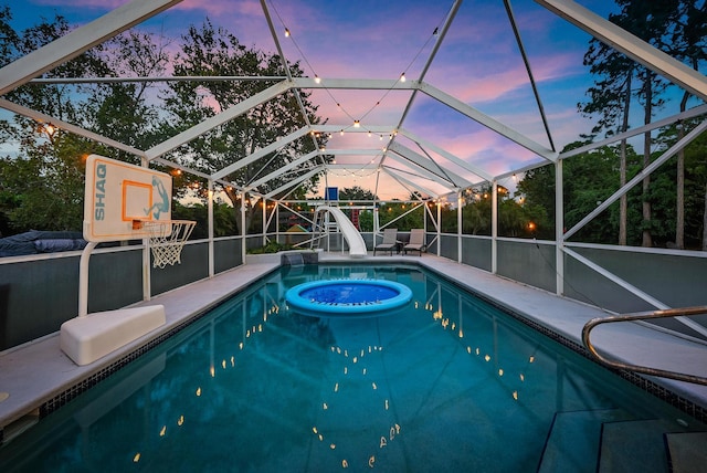 pool at dusk with a patio, glass enclosure, and a water slide