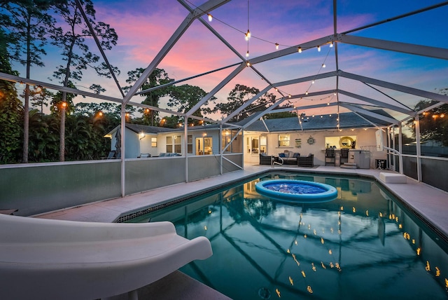 pool at dusk with a lanai, outdoor lounge area, and a patio