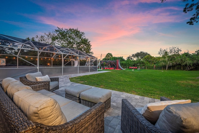 patio terrace at dusk featuring a lanai, a playground, a lawn, and an outdoor hangout area