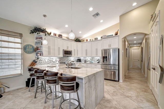 kitchen featuring appliances with stainless steel finishes, vaulted ceiling, sink, pendant lighting, and white cabinetry