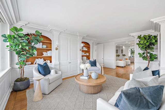 living room featuring light hardwood / wood-style floors, ornate columns, ornamental molding, and built in features