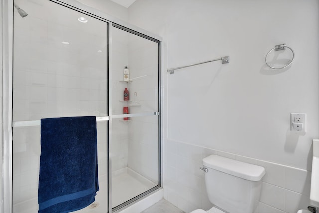 bathroom with toilet, a shower with door, and tile walls