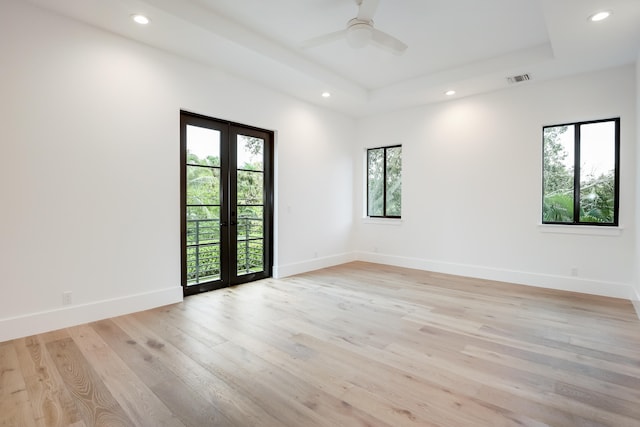 empty room with ceiling fan, light hardwood / wood-style floors, a tray ceiling, and french doors