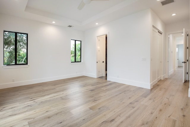 unfurnished room featuring a raised ceiling, ceiling fan, and light wood-type flooring