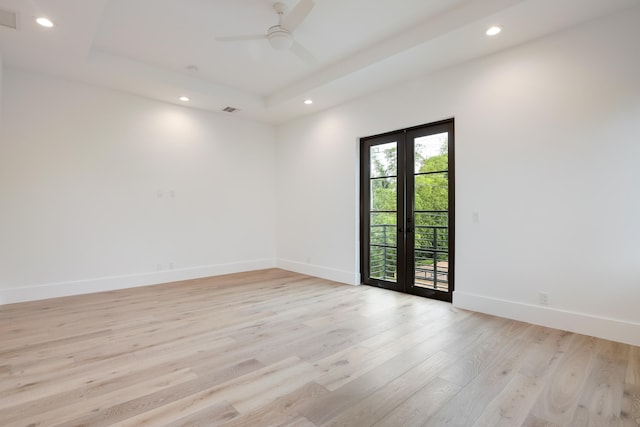 spare room with a tray ceiling, ceiling fan, french doors, and light wood-type flooring