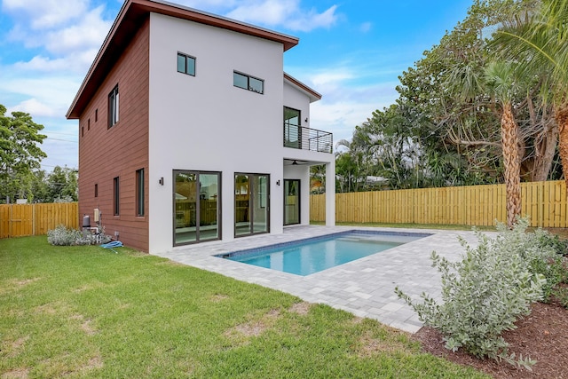 rear view of house featuring a fenced in pool, a balcony, a patio, and a lawn