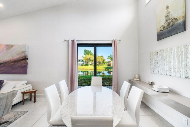 dining space featuring light tile patterned flooring, a water view, and a towering ceiling