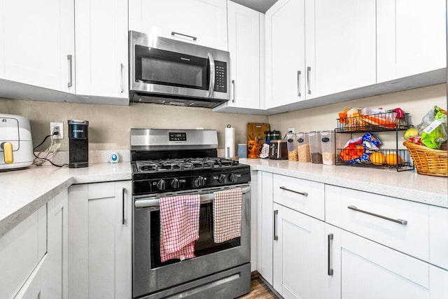 kitchen featuring light stone countertops, appliances with stainless steel finishes, white cabinetry, and wood-type flooring