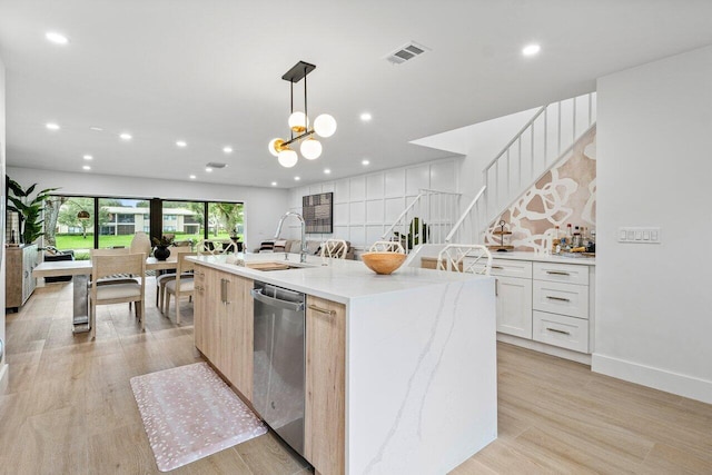 kitchen with pendant lighting, stainless steel dishwasher, sink, white cabinetry, and a kitchen island with sink