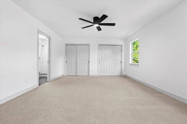 unfurnished bedroom featuring carpet, two closets, ensuite bathroom, and ceiling fan