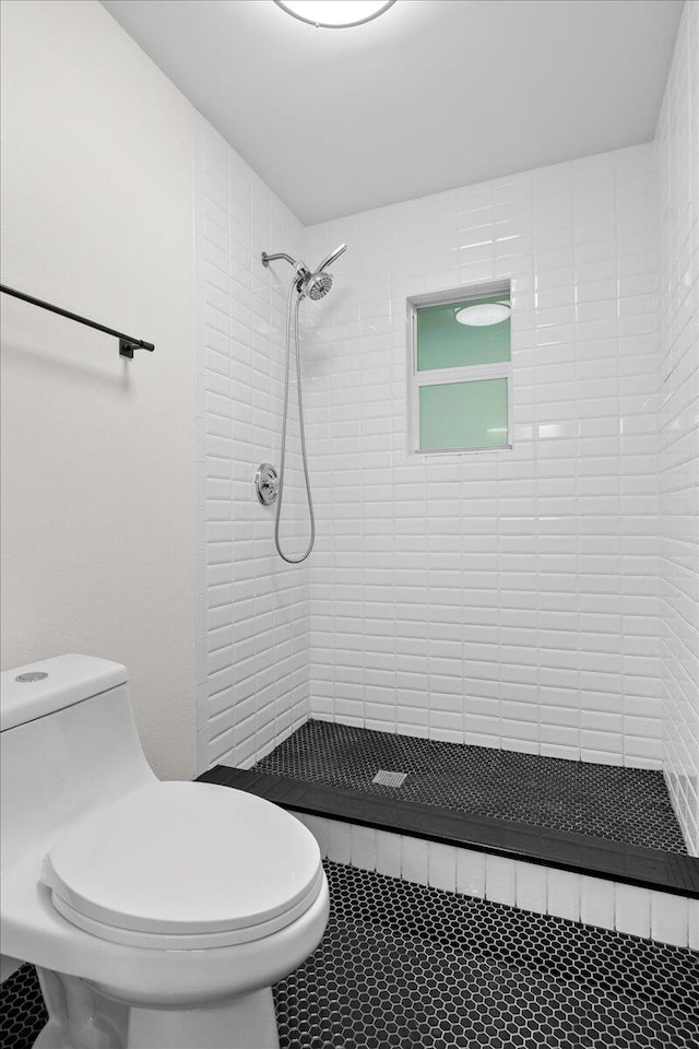 bathroom featuring toilet, a tile shower, and tile patterned floors