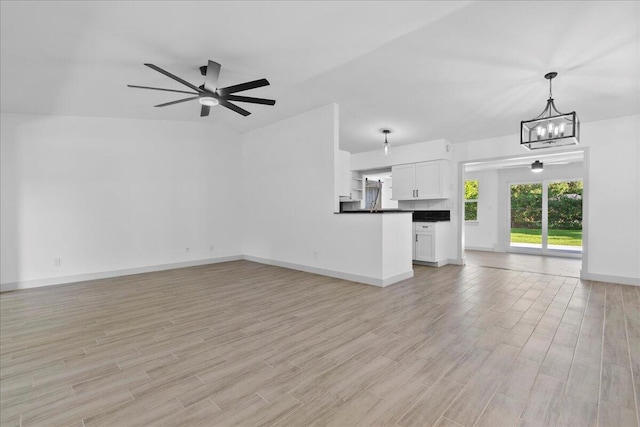 unfurnished living room featuring ceiling fan with notable chandelier and light hardwood / wood-style flooring