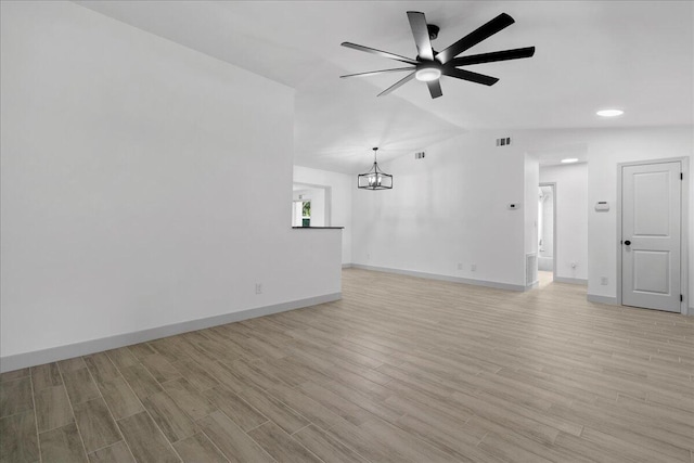 unfurnished living room with vaulted ceiling, ceiling fan with notable chandelier, and light wood-type flooring