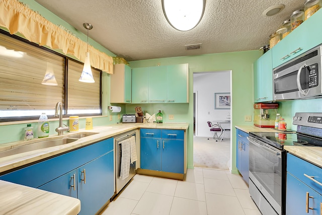 kitchen featuring sink, light tile patterned floors, a textured ceiling, decorative light fixtures, and stainless steel appliances