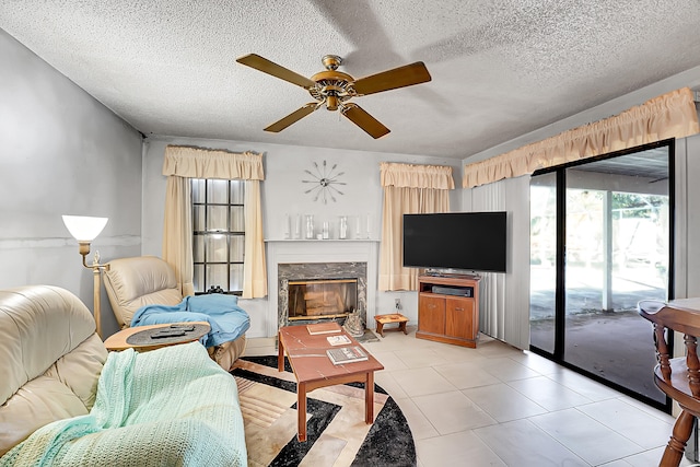 living room featuring a premium fireplace, ceiling fan, light tile patterned flooring, and a textured ceiling