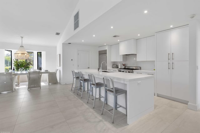 kitchen featuring a center island with sink, white cabinets, stove, hanging light fixtures, and light countertops