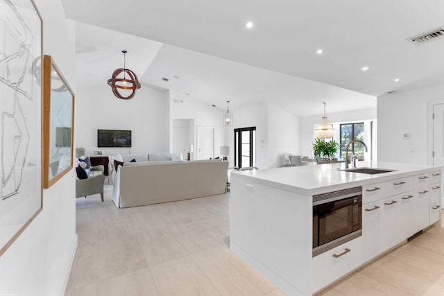 kitchen featuring light countertops, white cabinets, a sink, an island with sink, and built in microwave