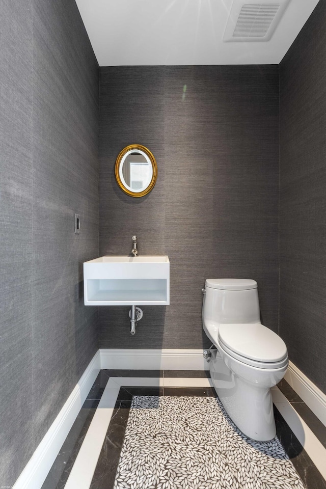 half bathroom featuring toilet, visible vents, baseboards, and a sink