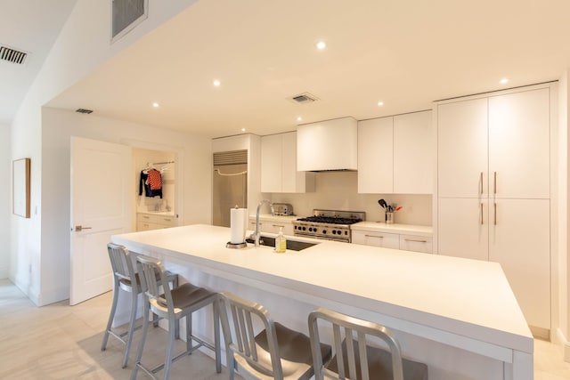 kitchen featuring custom exhaust hood, high quality appliances, a center island with sink, sink, and white cabinetry