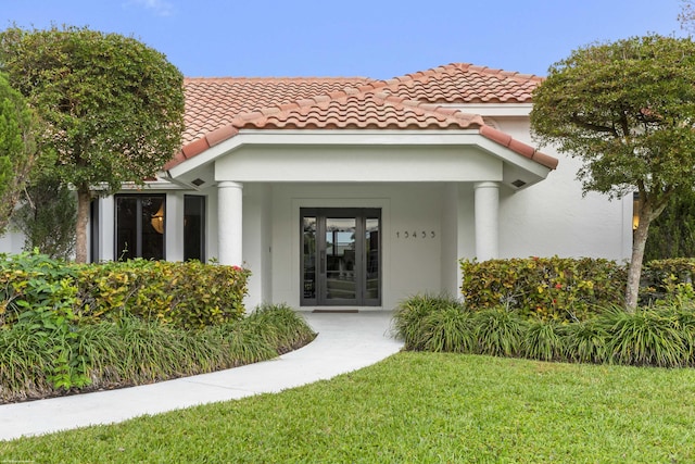 view of exterior entry featuring a tiled roof, a lawn, and stucco siding