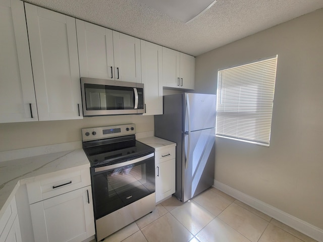 kitchen with white cabinetry, light stone countertops, a textured ceiling, light tile patterned floors, and appliances with stainless steel finishes