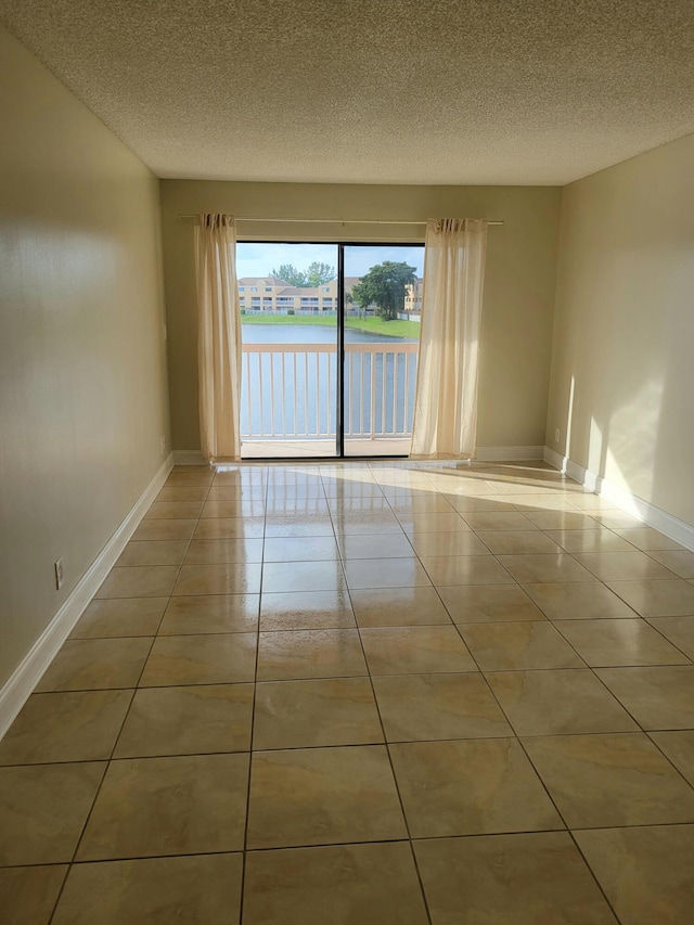 unfurnished room featuring light tile patterned floors, a textured ceiling, and a water view