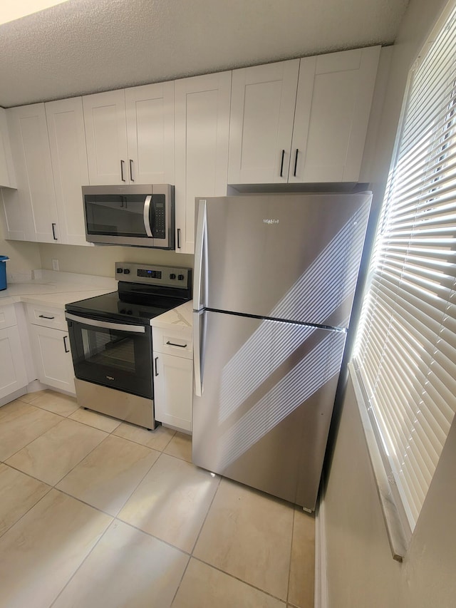 kitchen featuring a textured ceiling, white cabinets, light tile patterned floors, and appliances with stainless steel finishes