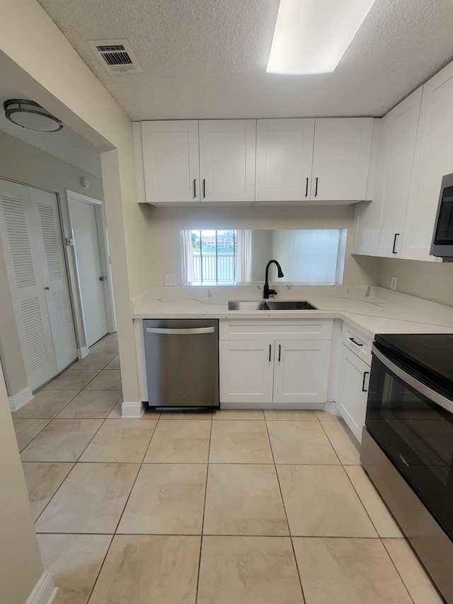 kitchen featuring white cabinets, sink, light tile patterned floors, a textured ceiling, and appliances with stainless steel finishes