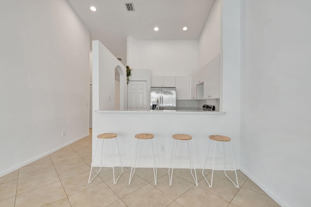 kitchen featuring kitchen peninsula, stainless steel fridge, white cabinets, a breakfast bar area, and light tile patterned flooring