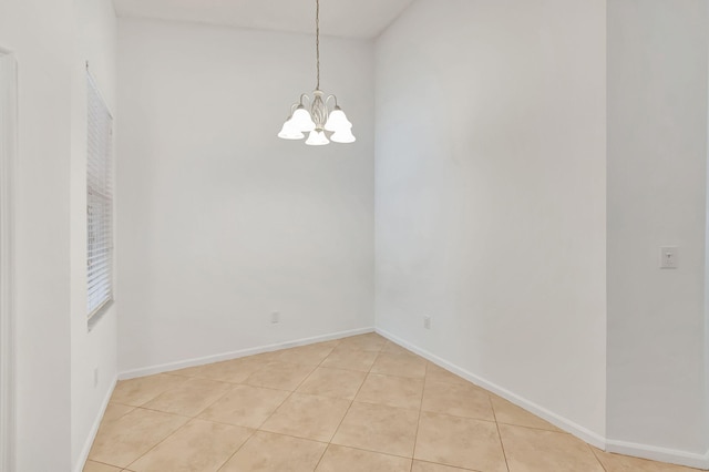 tiled spare room with a notable chandelier